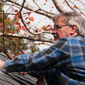 older man working on a roof, holding a hammer in his right hand