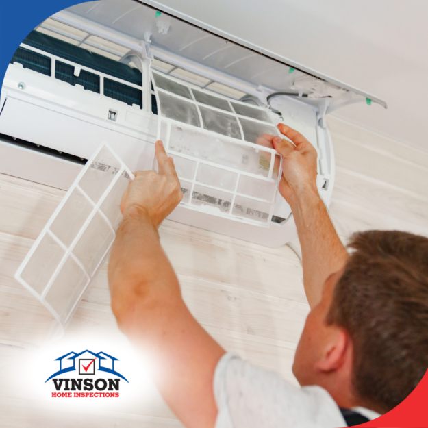 Vinson Home Inspections(1) A technician inspects and replaces the filter of a wall-mounted air conditioning unit inside a home with wooden paneling.