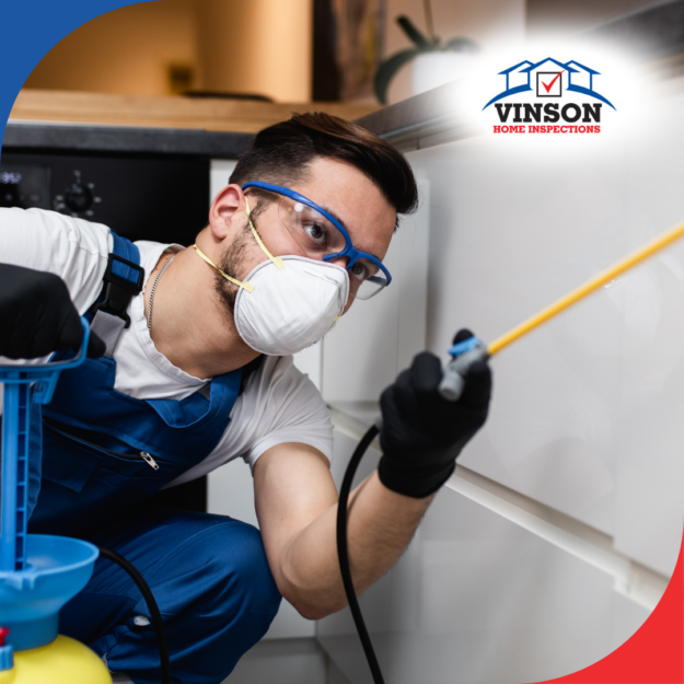 Pest control technician wearing protective gear spraying pesticide in a kitchen.
