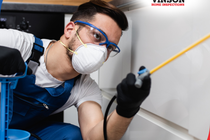 Pest control technician wearing protective gear spraying pesticide in a kitchen.