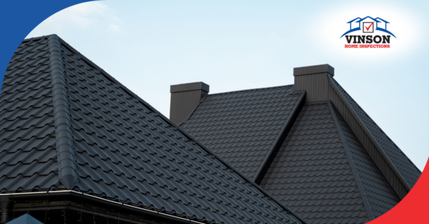 Close-up of a home's metal roof with ridges and chimneys under a clear sky.