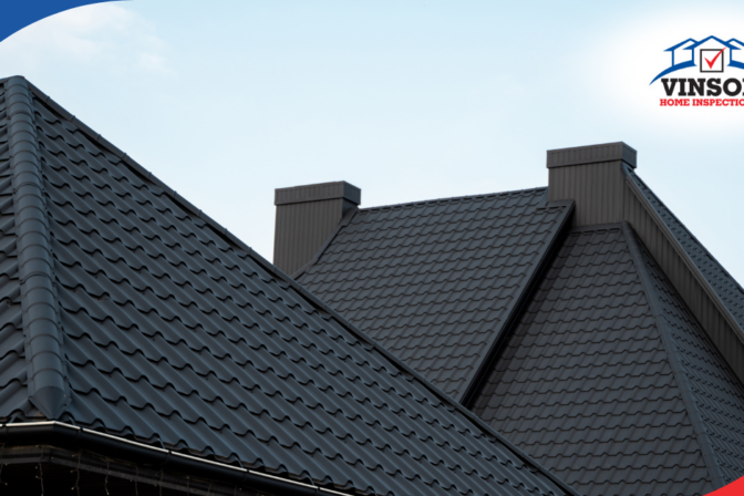 Close-up of a home's metal roof with ridges and chimneys under a clear sky.