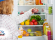 Woman placing berries in a refrigerator stocked with fruits, vegetables, and drinks.