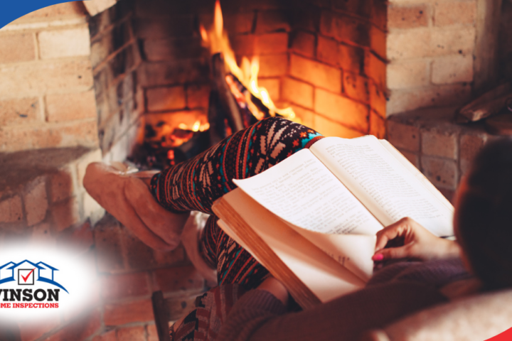 Person reading a book while sitting by a brick fireplace with a warm fire burning.