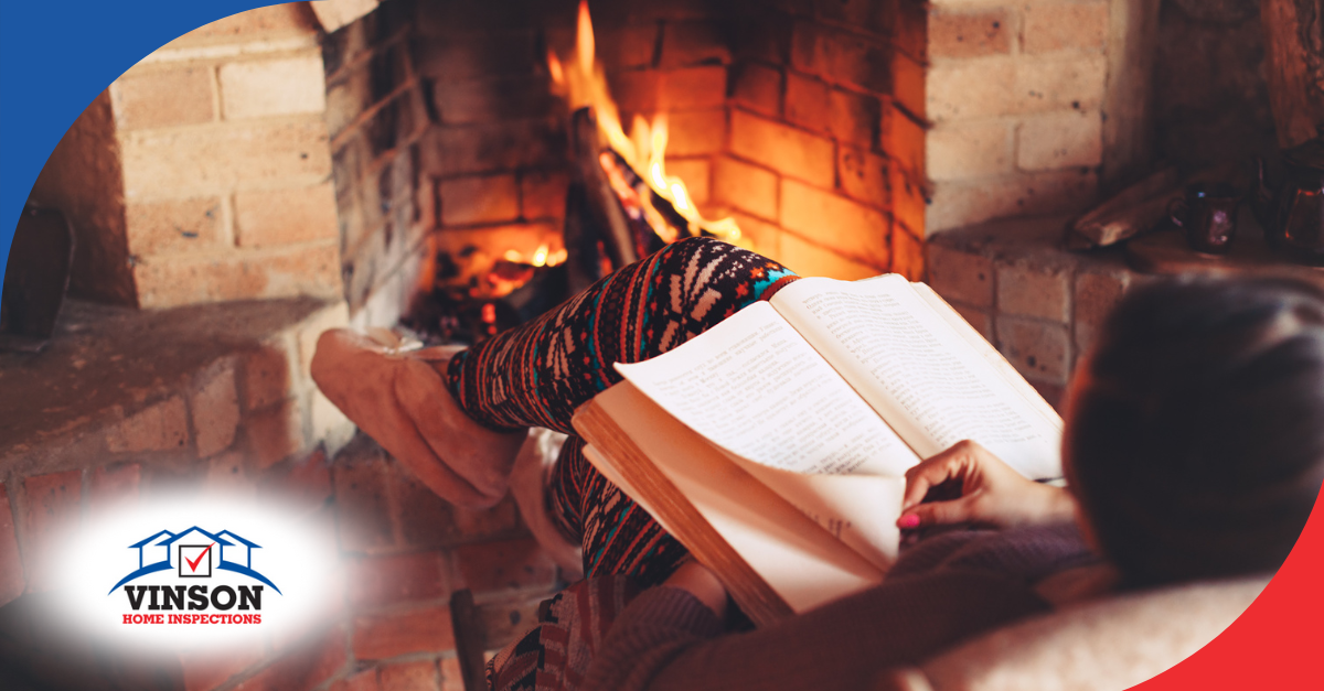 Person reading a book while sitting by a brick fireplace with a warm fire burning.