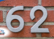 Gray house number 62 on a red brick wall