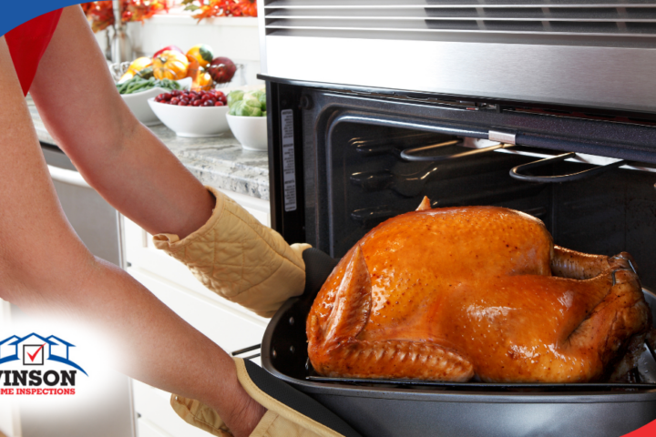 Person removing a golden roasted turkey from the oven, with a kitchen counter full of fresh produce in the background.