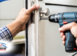 Person tightening a door latch with a power drill.